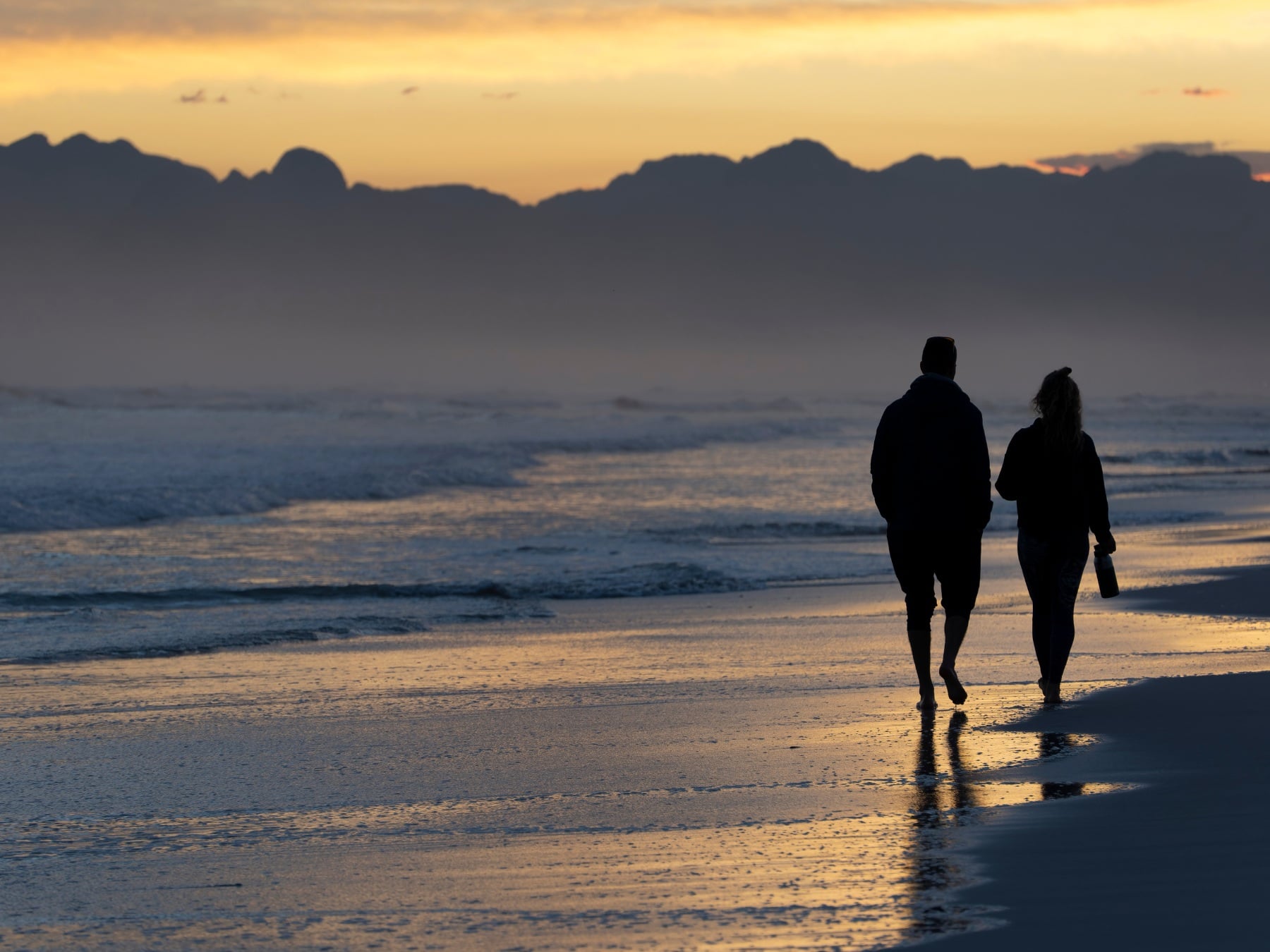 A couple walking by the ocean at sunset